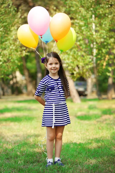 Happy little girl in striped dress with colourful balloons in the park — Stock Photo, Image