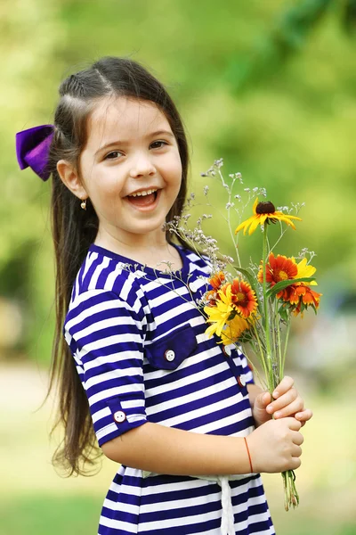 Portret szczęśliwy dziewczynki z kwiatami w parku — Zdjęcie stockowe