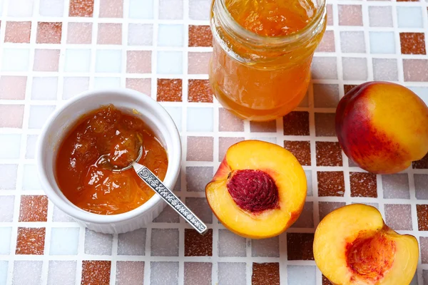 Tasty jam in the jar and bowl, ripe peaches on mosaic background close-up — Stock Photo, Image