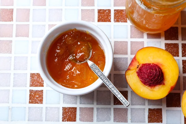 Вкусный джем в банке и чаше, спелые персики на мозаичном фоне крупным планом — стоковое фото