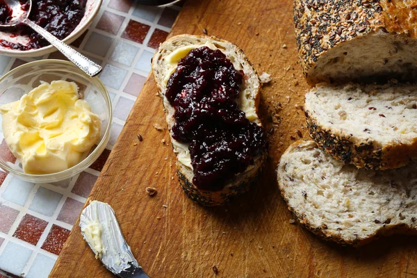 Heerlijke jam op de plaat, boter, vers brood en houten tablet op mozaïek achtergrond — Stockfoto