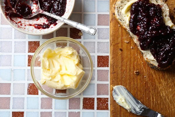 Tasty jam on the plate, butter, fresh bread and wooden tablet on mosaic background — Stock Photo, Image