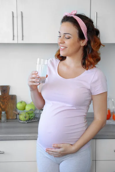 Mulher grávida atraente bebe água na cozinha — Fotografia de Stock