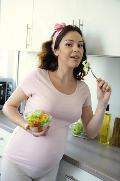 Mulher grávida atraente come salada de vitamina na cozinha — Fotografia de Stock