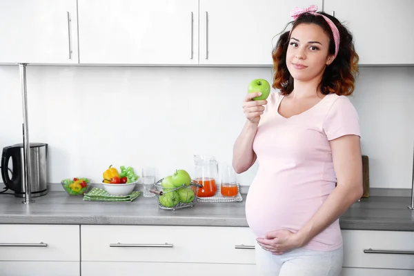 Joven mujer embarazada feliz con manzana en la cocina —  Fotos de Stock