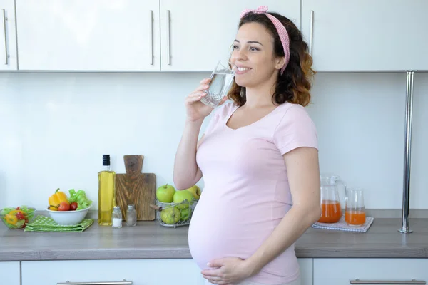 Mulher grávida atraente bebe água na cozinha — Fotografia de Stock