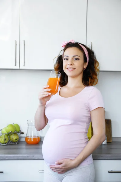 Jovem mulher grávida feliz com copo de suco na cozinha — Fotografia de Stock