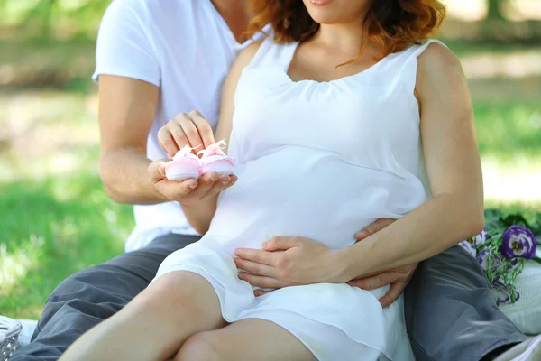 Hombre guapo y su encantadora esposa embarazada con botines de bebé en el parque, de cerca —  Fotos de Stock