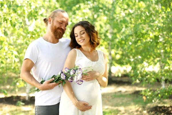 Un bel homme donne un bouquet de jolies fleurs à sa charmante femme enceinte dans le parc — Photo