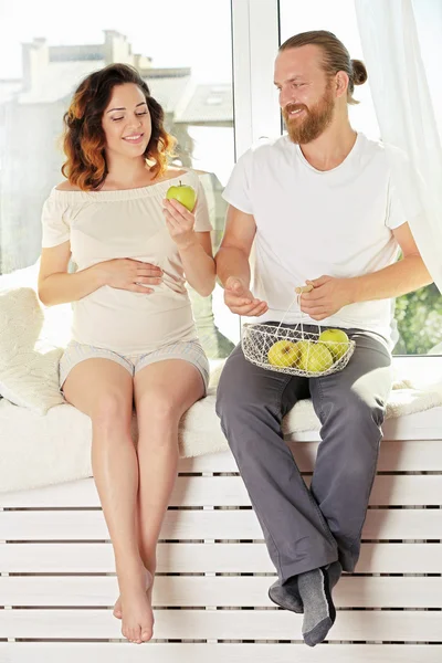 Feliz pareja amada en espera del nacimiento del bebé en el tablero de la ventana con manzanas — Foto de Stock