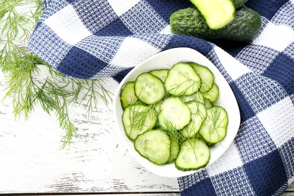 Gesneden komkommers op wit bord met blue gecontroleerd katoen servetring — Stockfoto