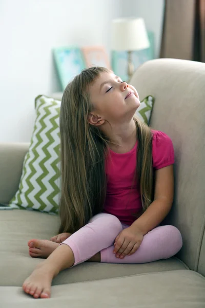 Vacker liten flicka sitter på soffan, på hem inredning bakgrund — Stockfoto