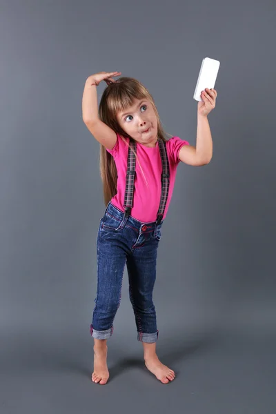 Красивая маленькая девочка с мобильным телефоном, на сером фоне — стоковое фото