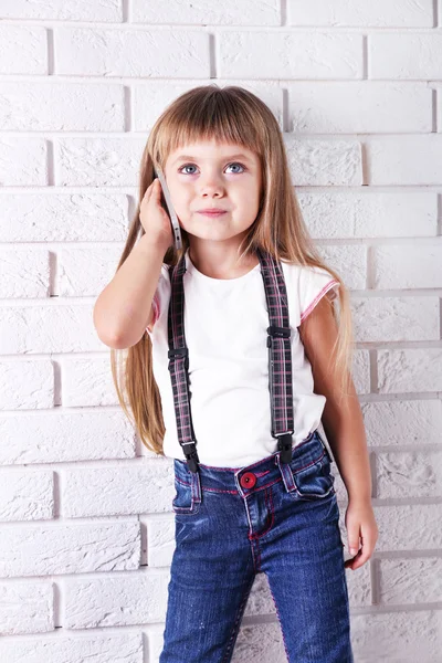 Schönes kleines Mädchen mit Handy auf hellem Wandhintergrund — Stockfoto