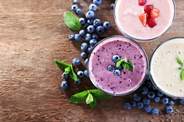 Sabrosos yogures de arándanos, fresas y leche con bayas y menta sobre fondo de madera — Foto de Stock