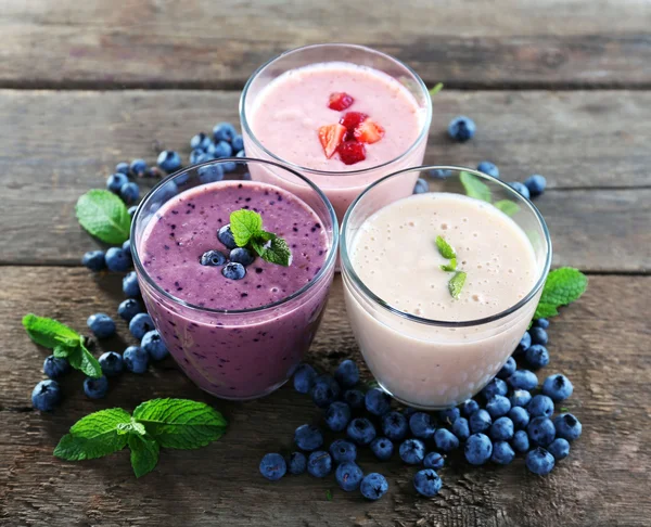 Sabrosos yogures de arándanos, fresas y leche con bayas y menta sobre fondo de madera — Foto de Stock