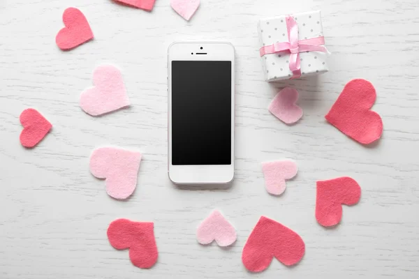 Teléfono inteligente con pantalla en blanco y corazones en mesa de madera — Foto de Stock