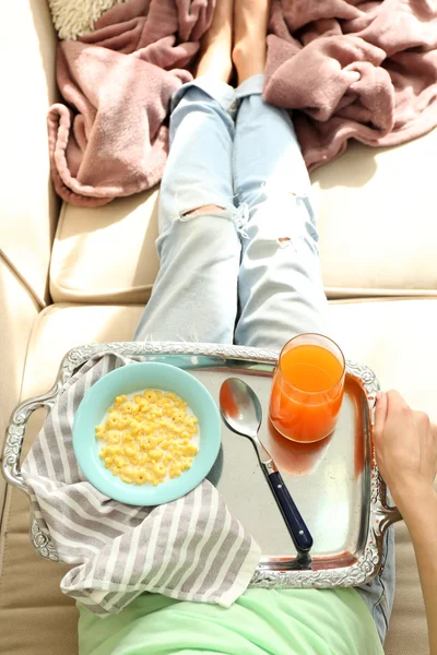 Chica con una bandeja almorzando en un sofá — Foto de Stock