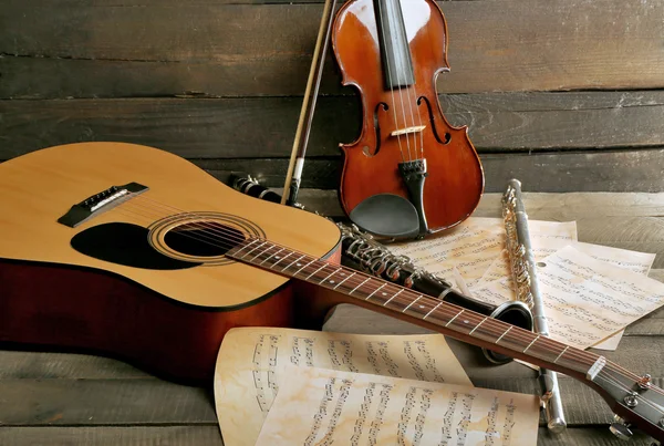 Акустическая гитара, сопрано-саксофон, скрипка, флейта и нотные листы на деревянном фоне — стоковое фото