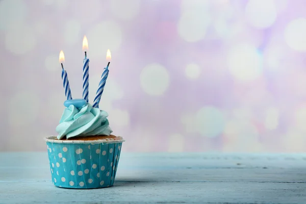 Sweet cupcake with candles on blue wooden table against blurred background — Stock Photo, Image