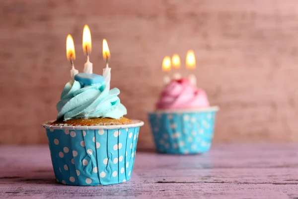 Sabrosos cupcakes con velas sobre mesa violeta sobre fondo de madera —  Fotos de Stock