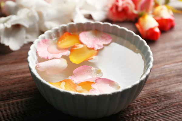 Rosa y naranja pétalos de rosa en un tazón de agua sobre fondo de madera — Foto de Stock