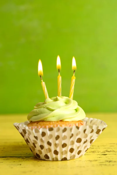 Leckerer Cupcake mit Kerzen auf gelbem Holztisch vor grünem Hintergrund — Stockfoto