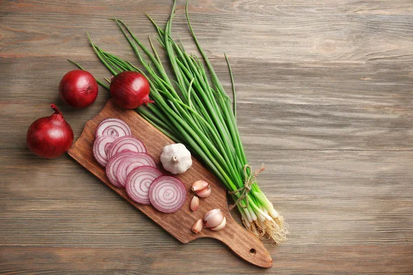 Círculos de cebollas rojas, cebolla verde con ajo a bordo sobre fondo de madera — Foto de Stock