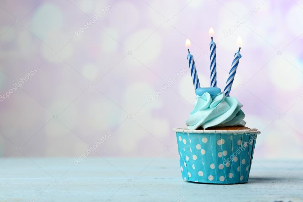 Sweet cupcake with candles on blue wooden table against blurred background