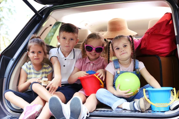 Trois belles filles et un garçon assis sur un coffre de voiture et riant — Photo