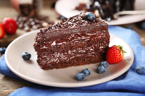 Шоколадный торт со сливками и свежими ягодами на тарелке, на деревянном фоне — стоковое фото