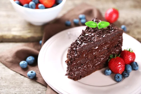 Schokoladenkuchen mit Schokoladencreme und frischen Beeren auf Teller, auf Holzgrund — Stockfoto