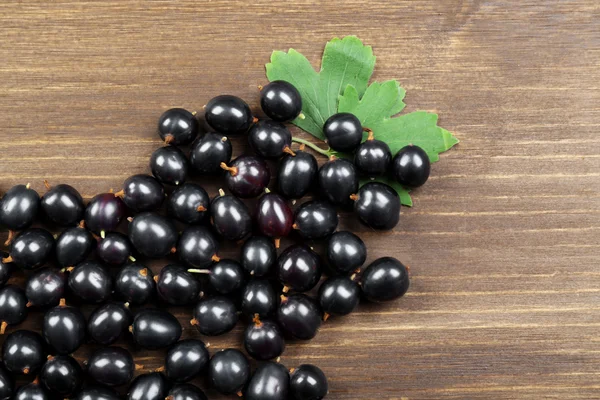 Heap of wild black currant with green leaves on wooden table close up — Stock Photo, Image