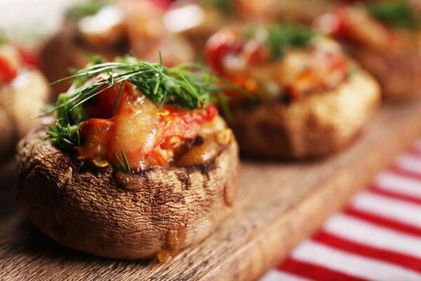 A wooden tablet with stuffed mushrooms and vegetables on the table, close-up