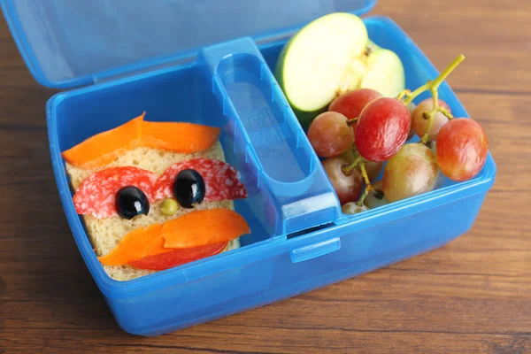 Creative sandwich and fruits in plastic lunchbox on wooden background — Stock Photo, Image