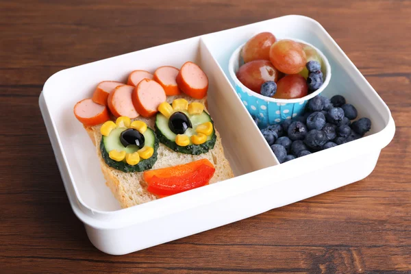 Creative sandwich with fruits in lunchbox on wooden background — Stock Photo, Image