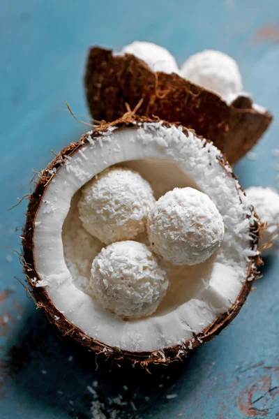 Bonbons in Kokosflocken und frischen Kokosnüssen auf farbigem Holzhintergrund — Stockfoto