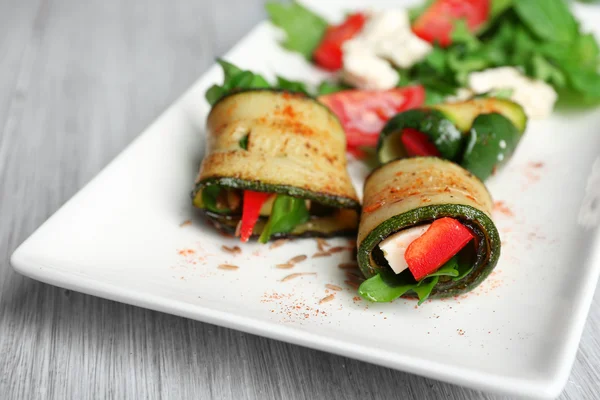 Rotoli di zucchine con formaggio, peperoni e rucola sul piatto, primo piano, sullo sfondo della tavola — Foto Stock