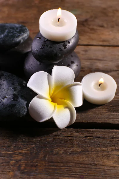 Relaxing composition with exotic fragipani flower, pebbles and candles on wooden background — Stock Photo, Image