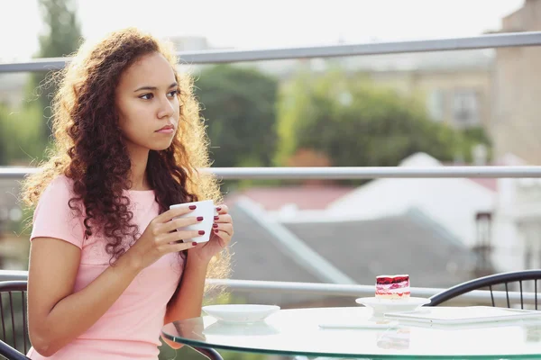 Hübsche junge Frau in rosa Kleid trinkt Kaffee auf Sommerterrasse — Stockfoto