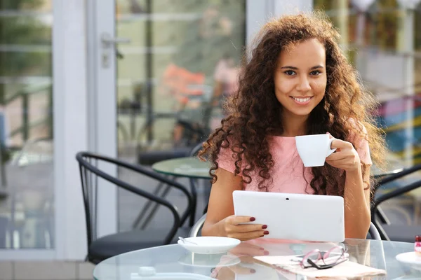 Hermosa joven con la tableta sentada en la terraza de verano y beber café — Foto de Stock
