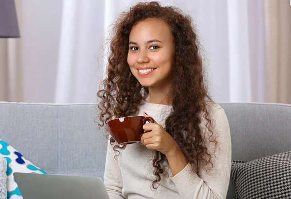 Joven hermosa mujer en el sofá utilizando el ordenador portátil y beber café en la habitación — Foto de Stock