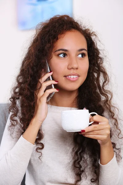 Nahaufnahme Porträt einer jungen Frau, die mit einer Tasse Kaffee im Zimmer telefoniert — Stockfoto