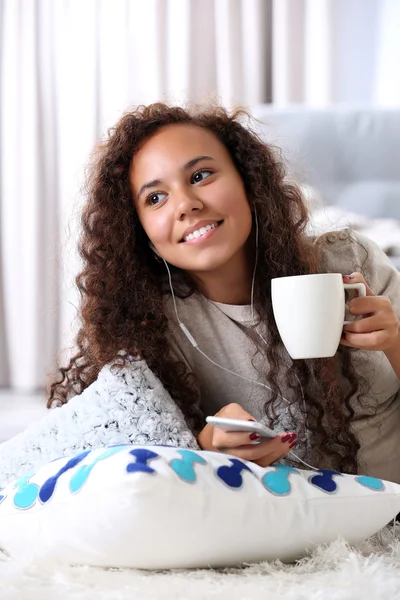 Beautiful girl listening music by headphones with cup of coffee in hands