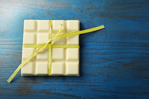 Barra di cioccolato bianco con fiocco colorato su sfondo di legno colore — Foto Stock