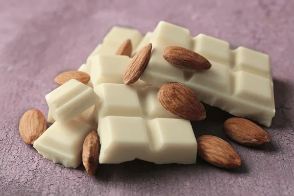 Части белого шоколада с орехами на фоне цвета дерева — стоковое фото