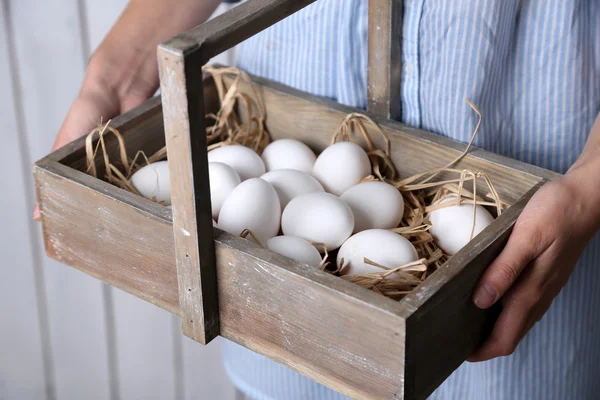 Huevos en cesta en las manos de las mujeres sobre fondo de madera —  Fotos de Stock