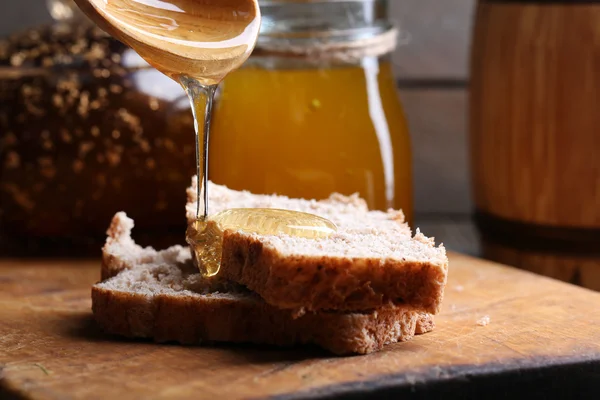 Mel pingando no pão fresco no fundo de madeira — Fotografia de Stock