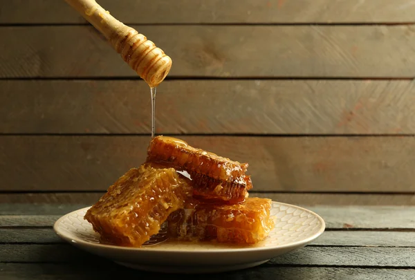 Miel goteando en panales, sobre fondo de madera — Foto de Stock