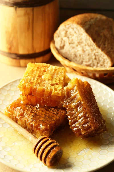 Panales de abeja y cazo de madera en plato, pan fresco en canasta sobre fondo de madera — Foto de Stock